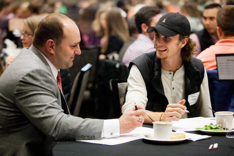man wearing gray suit speaking with a student at a mentorship event