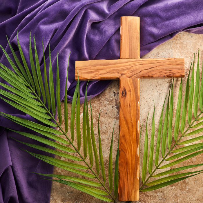 A wooden cross laying on a table draped in purple fabric and a bed of palms