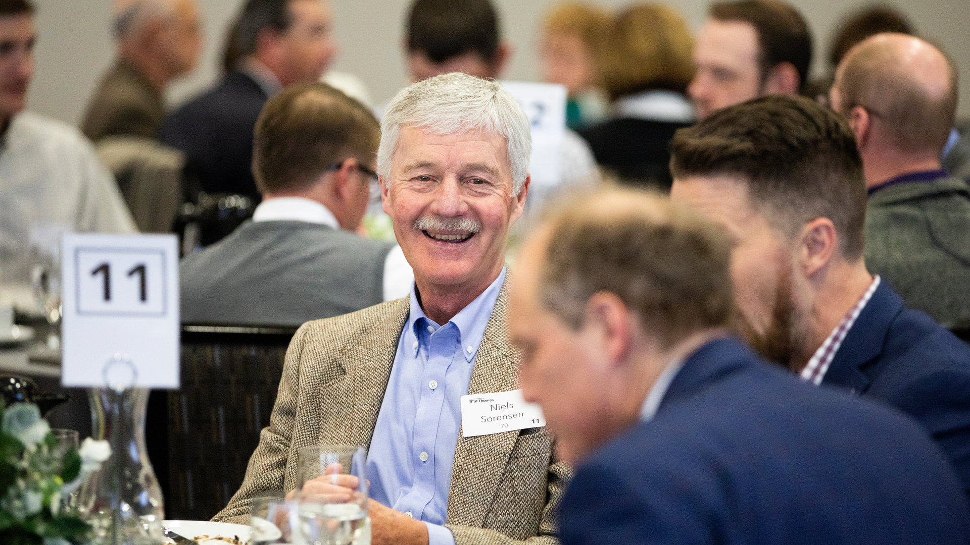 Man smiles at an event with alumni.