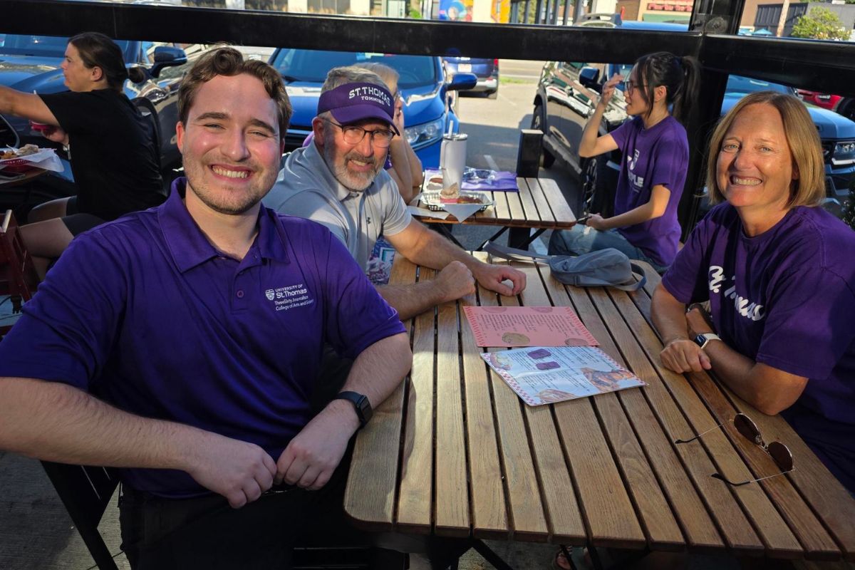 four people smiling and wearing St. Thomas gear pose for a photo