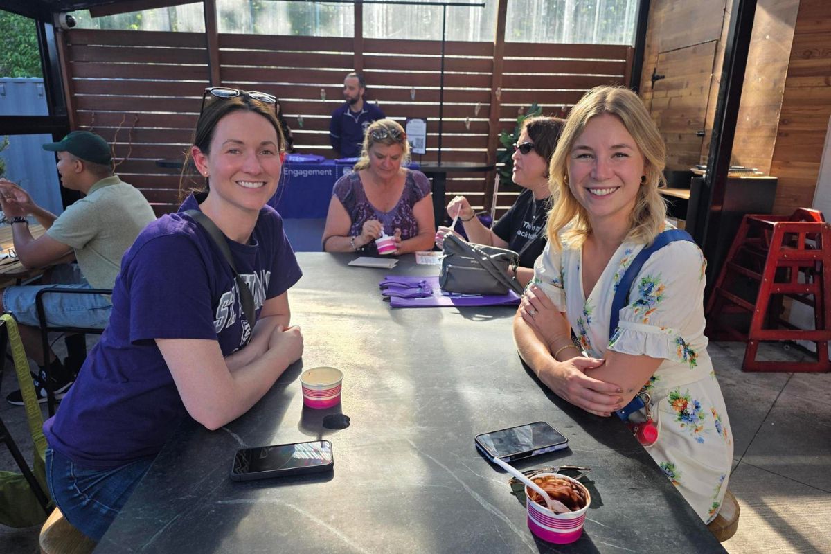 two friends at a patio table smile for a photo