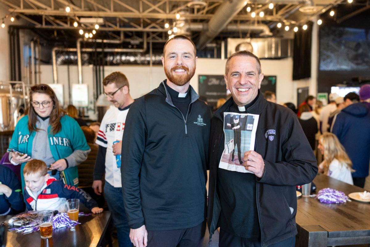 Father Chris poses with a Tommie and holds a photo of his uncle throwing the first pitch at a Twins game