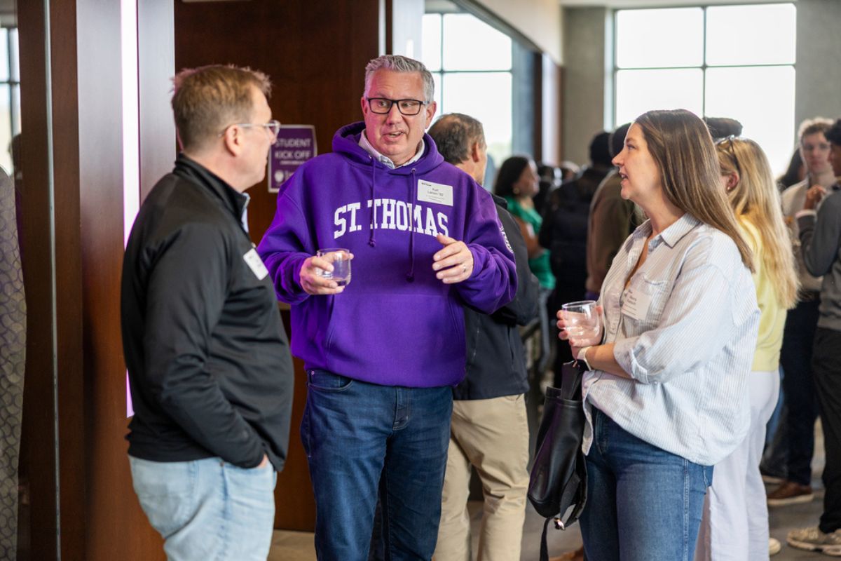 A Tommie alumni speaks animatedly with Tommie students outside Woulfe Alumni Hall
