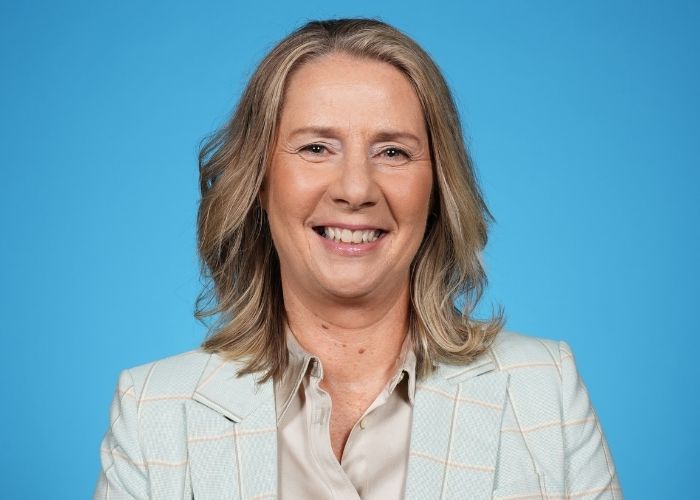 Cheryl Reeve wears a grey suit and smiles for a studio portrait against a white background