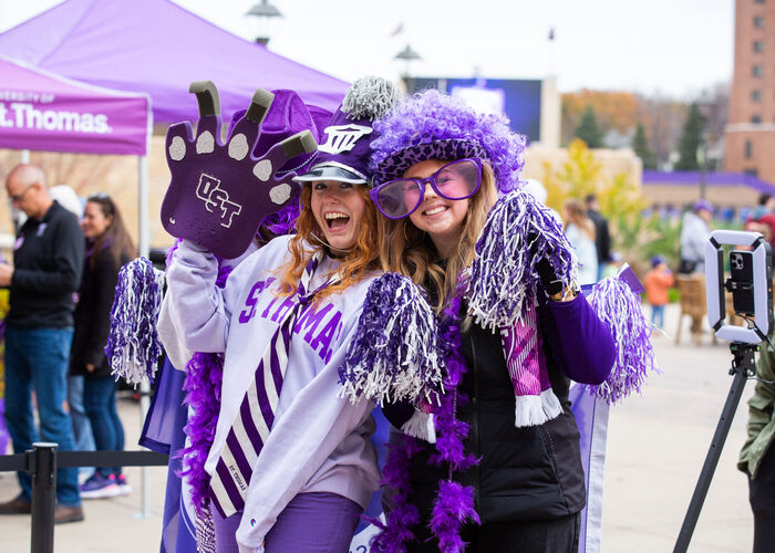 Two Tommies don fun purple gear at Homecoming 2024. They’re wearing feathery cowboy hats, giant sunglasses, and purple zebra stripes.