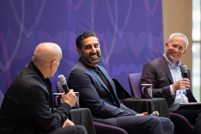 Marc Lore, Vik Uppal and President Vischer speak animatedly from chairs on a stage in front of a purple fabric background