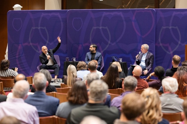 A crowd of attendees watches as Marc Lore speaks to Vik Uppal and President Vischer