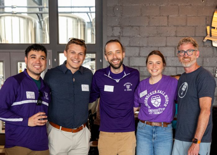 Five Tommie alumni in St. Thomas purple smile for a group photo taken in the taproom at Insight Brewing.