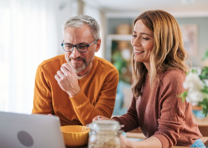 A couple smile while viewing a laptop screen.