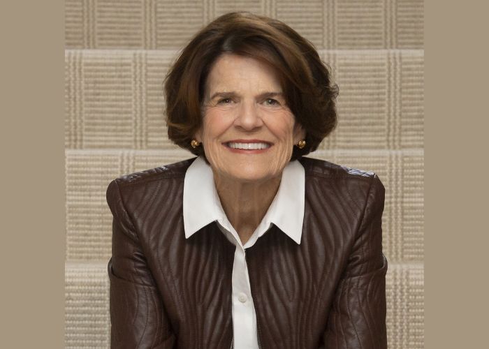 Penny George ’95 smiles into the camera while sitting on a set of brown stone steps