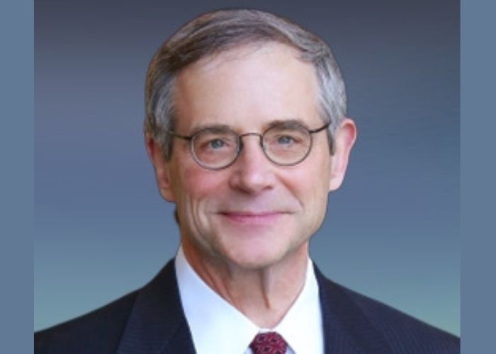 Dr. John P. Knoedler ’73 wears a suit and smiles into the camera against a blue background
