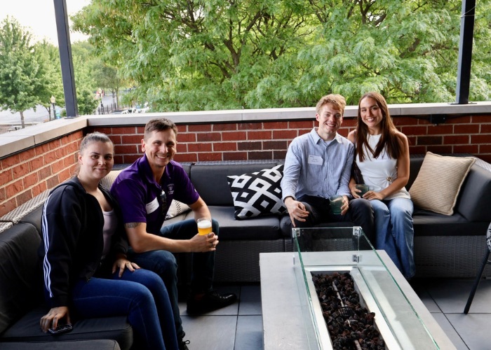 A family wearing St. Thomas gear smiles for a photo from a patio sofa at The Elm