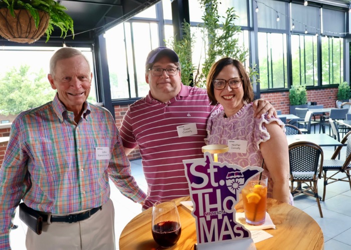 Three Tommies smile with their arms around each other at a table with St. Thomas decor