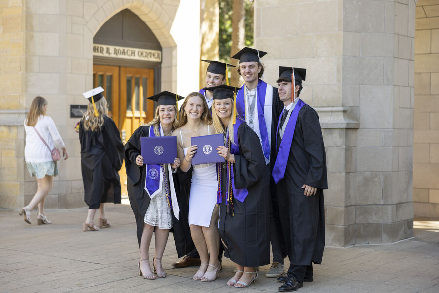 Students pose for a photo under Arches in their caps and gowns