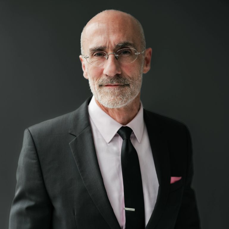 Arthur Brooks wears a grey suit and poses against a brown background for a studio portrait