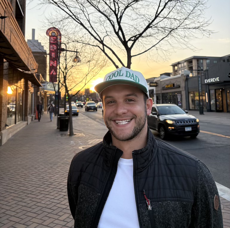 Bryce smiles into the camera in front of an urban outdoor background