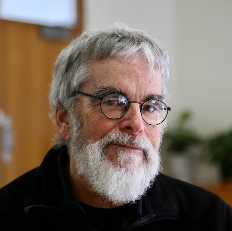 Br. Guy looking into the camera. He wears glasses and a black shirt.