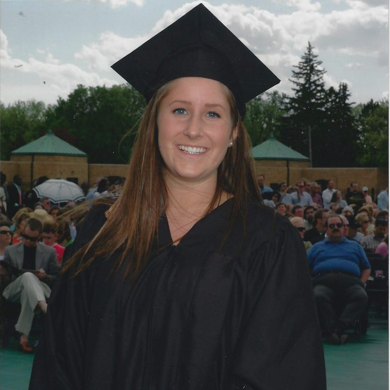 Krystal Julius wears a cap and gown. She smiles into the camera for a photo taken at a graduation ceremony