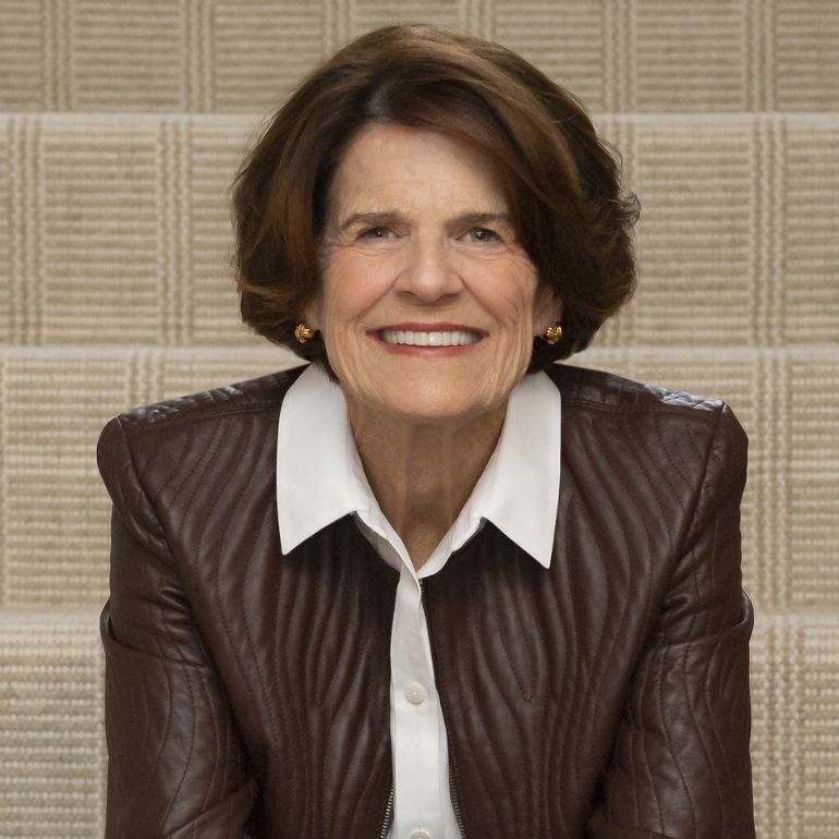 Penny George ’95 smiles into the camera while sitting on a set of brown stone steps