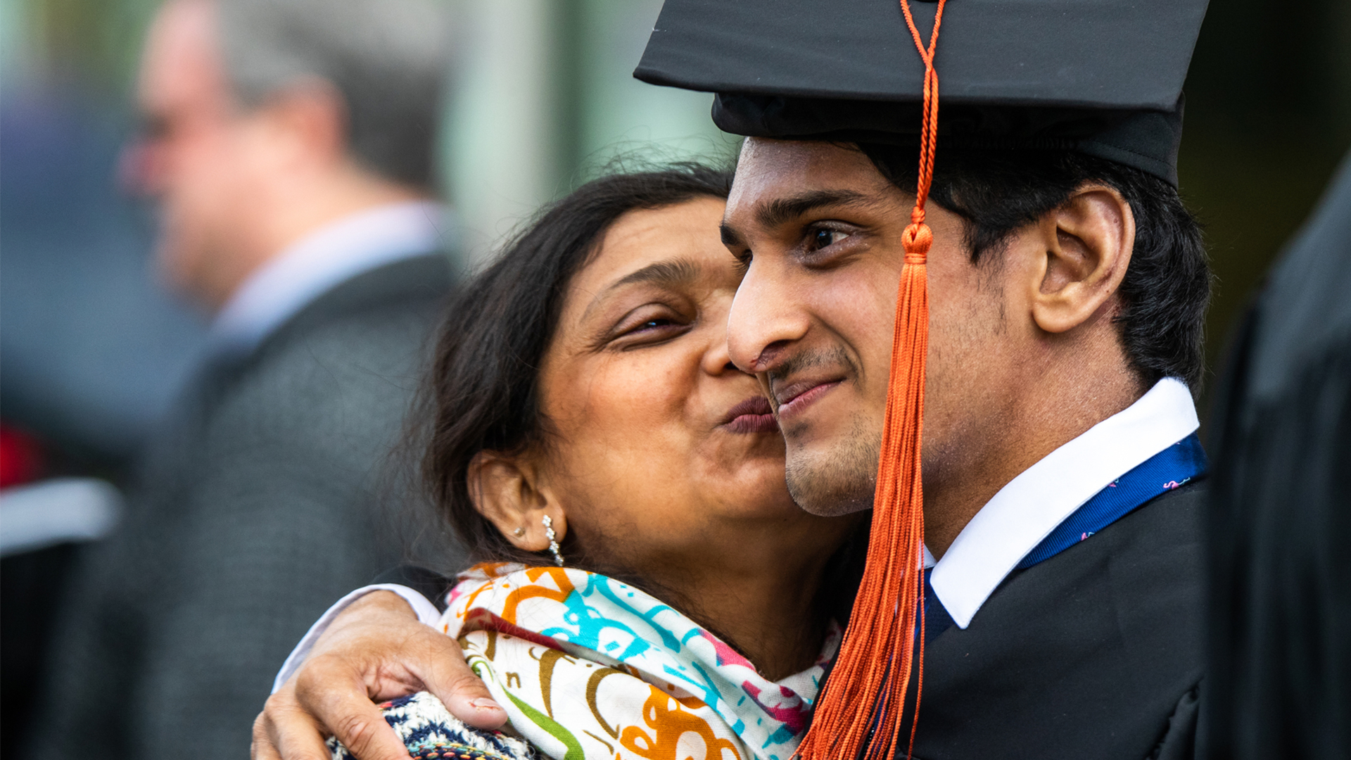 A mother kissing her son who is in his commencement robe and hat